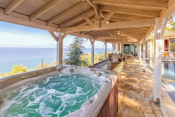 A hot tub with a stone exterior, wooden deck, and a view of the sea.