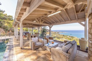 A covered outdoor seating area with wicker furniture, a pool, and a view of the sea.