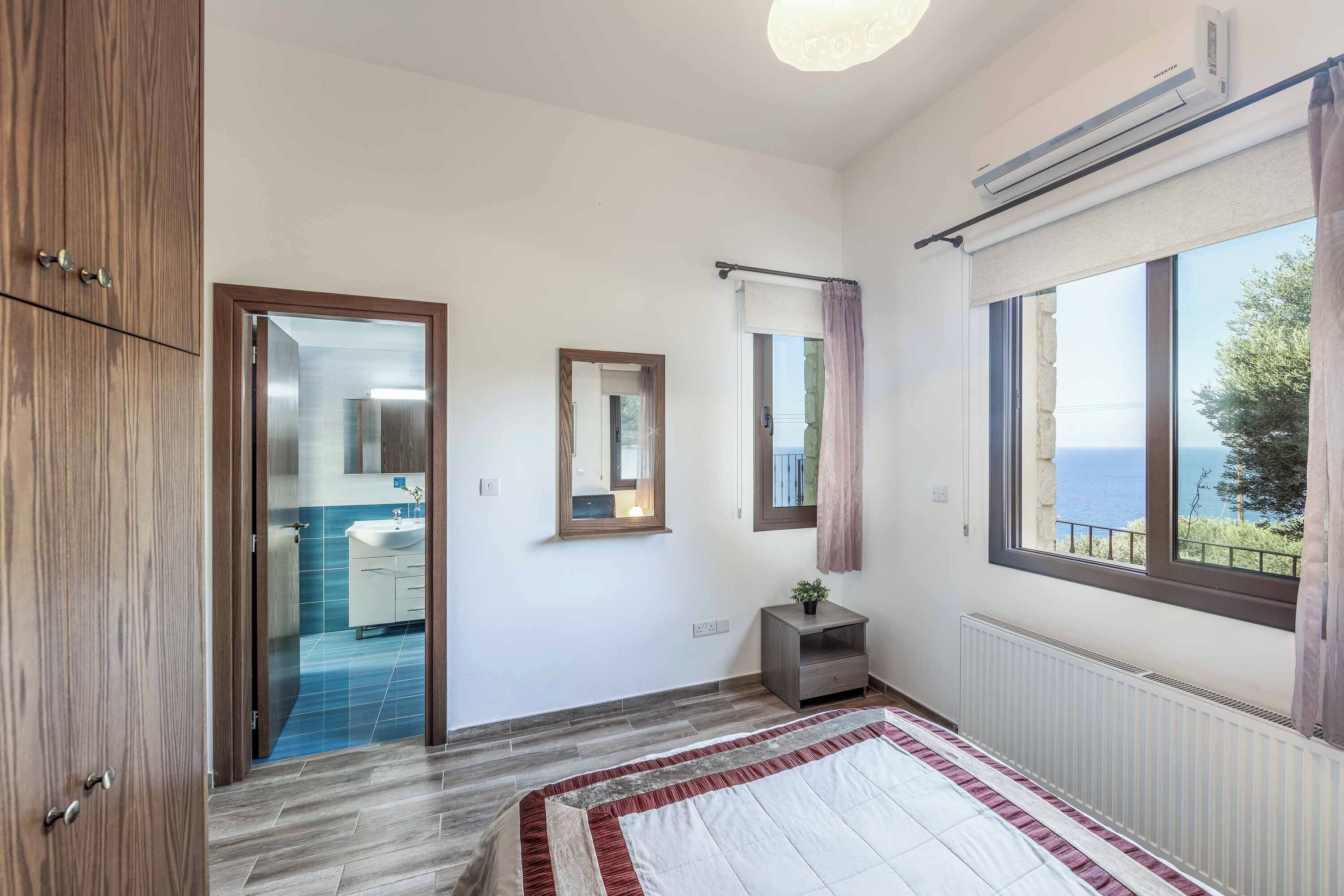 Un dormitorio con cama, ventana con vistas, radiador y puerta que da a un baño.