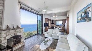 A spacious living area with a stone fireplace, white sofas, and a large window overlooking the sea. - Pomos View (Pomos)