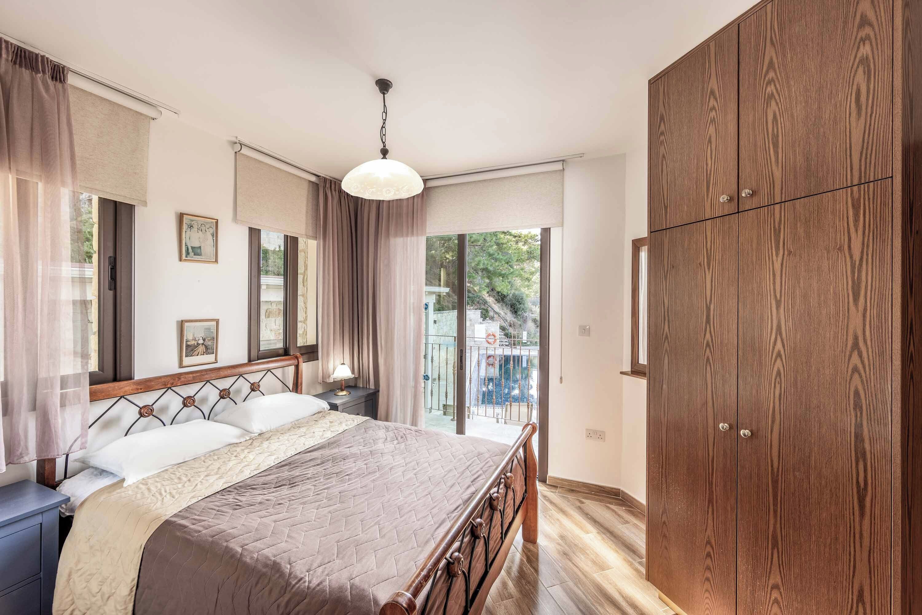 A bedroom with a bed, wooden wardrobe, and a balcony with a view.