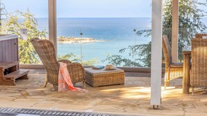 A sunlit outdoor seating area with wicker furniture, a pool, and a view of the sea. - Pomos View (Pomos)