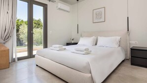 Un dormitorio moderno con una cama grande, una mesita de noche, una pequeña mesa con un florero y una puerta corrediza de vidrio que da a un espacio al aire libre.