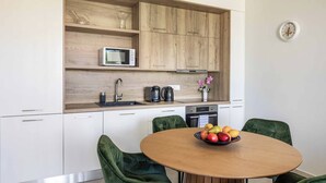 Una cocina moderna con armarios blancos, encimera de madera y una mesa redonda con sillas tapizadas de verde.