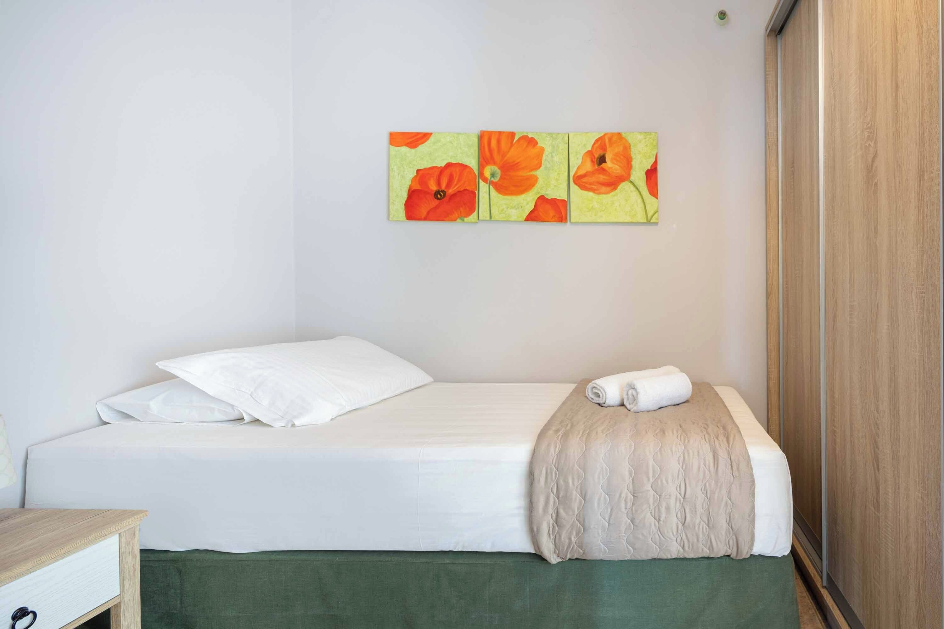 Een eenpersoonsbed met witte lakens, een groen bedbank en een beige deken.