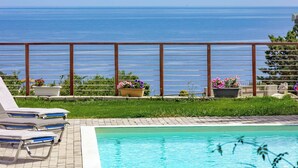 Zona de piscina con sillones de descanso y macetas, con vistas a una extensión de agua.