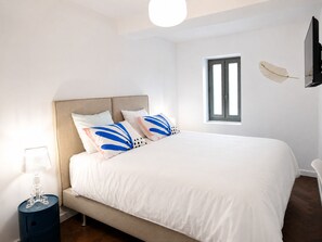 A bedroom with a bed, a nightstand, a lamp, a window, and a wall-mounted TV. - Elegant Provençal Wine Estate Surrounded by Vineyards (Le Muy)