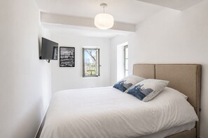 A bedroom with a bed, a television mounted on the wall, and a window.