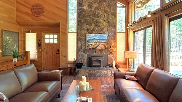 Un intérieur de chalet chaleureux avec une cheminée en pierre, des canapés en cuir et de grandes fenêtres.