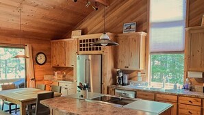 Une cuisine spacieuse avec des meubles en bois, un grand îlot central doté de tabourets, un réfrigérateur et une fenêtre laissant entrer la lumière naturelle.