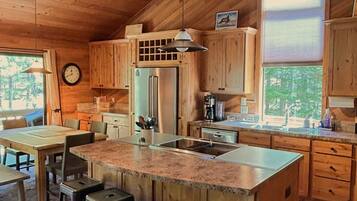 A spacious kitchen with wooden cabinets, a large island with bar stools, a refrigerator, and a window providing natural light.
