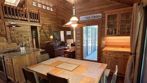 L’intérieur d’un chalet en bois comprend un coin repas, une cuisine et un panneau indiquant « Restaurant en plein air de l’hôtel Sisters ».