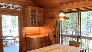 Un coin repas en bois, avec une table et des chaises, un luminaire suspendu et une vue sur l’extérieur.
