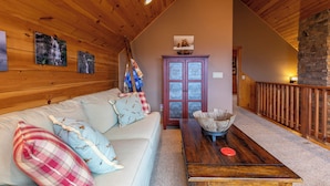 A cozy loft-style room with a wooden ceiling, a sofa with patterned cushions, a wooden coffee table, and a stone fireplace. - Deer Moments (Banner Elk)