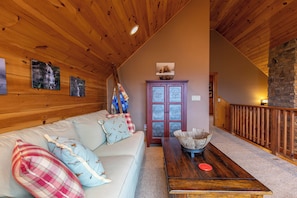 Ein gemütlicher Loftraum mit Holzbalkendecke, einer Couch mit gemusterten Kissen, einem Holztisch und einem Steinkamin.