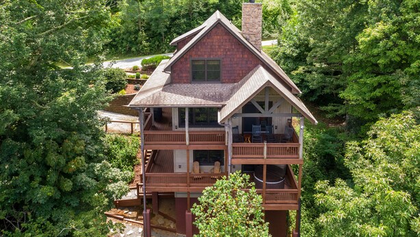 A two-story wooden house with a balcony, surrounded by dense forest. - Deer Moments (Banner Elk)
