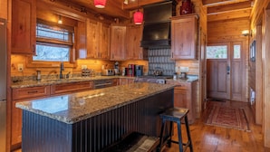 A spacious kitchen with wooden cabinets, granite countertops, and a central island with stools. - Deer Moments (Banner Elk)