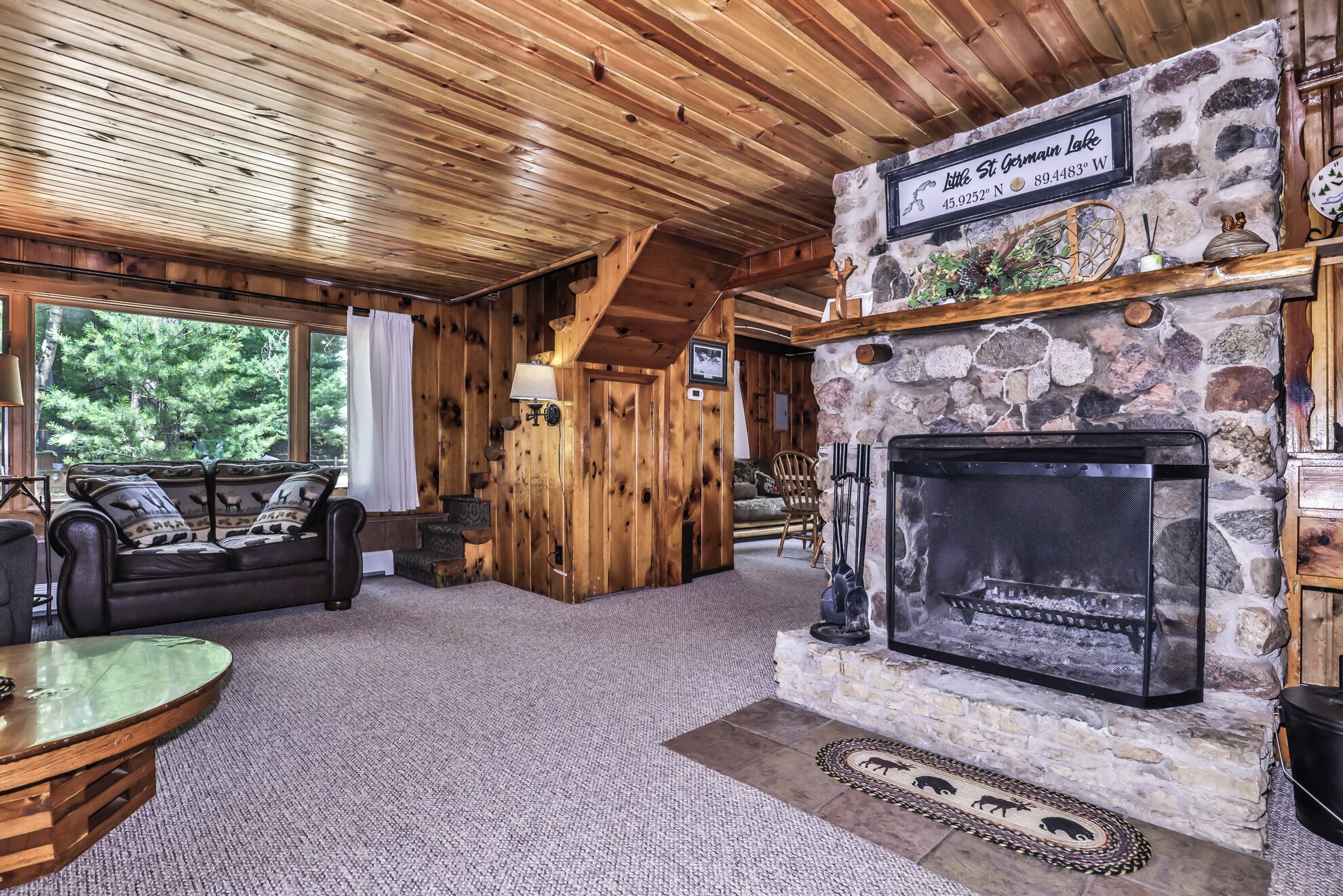A cozy cabin interior with a stone fireplace, wooden walls, and a comfortable seating area with a view of the outdoors.