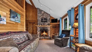 A log cabin interior with a stone fireplace, wooden walls, and a cozy seating area.