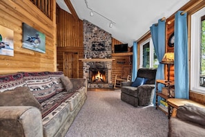 L’intérieur d’une cabane en rondins, avec une cheminée en pierre, des murs en bois et un coin salon confortable.