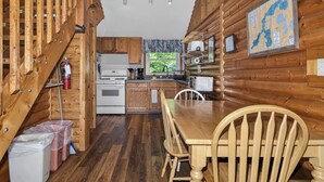 A wooden cabin interior with a kitchen, dining table, and chairs.