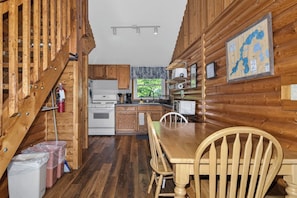 Interior de una cabaña de madera con cocina, mesa y sillas.