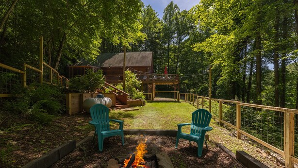 Eine Holzterrasse mit zwei grünen Adirondack-Stühlen vor einem Feuerkorb.