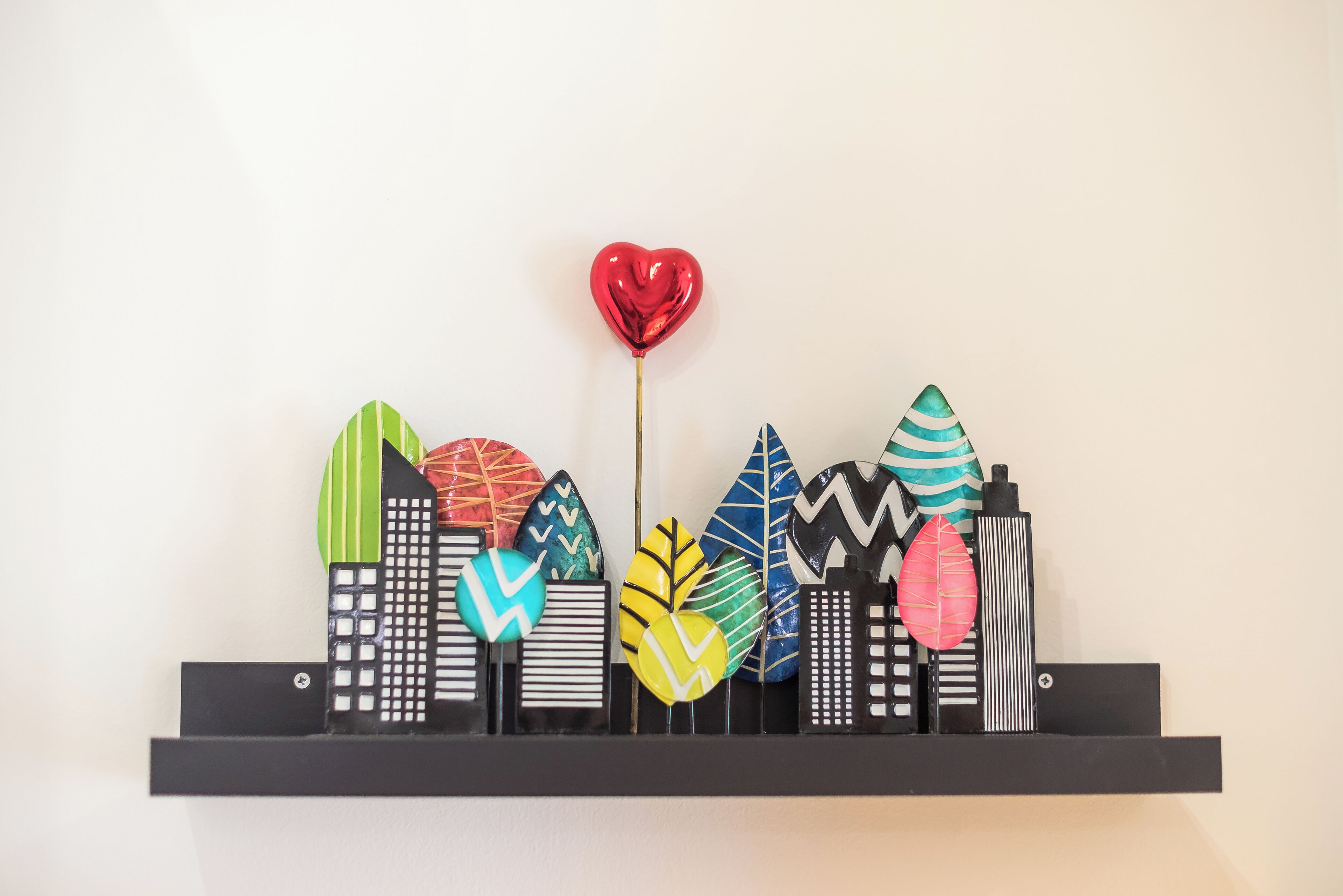 Un panneau mural présentant des formes architecturales abstraites et colorées, agrémenté d’un ballon en forme de cœur rouge.