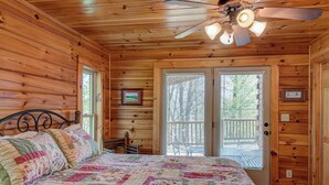 A wooden cabin bedroom with a bed, a ceiling fan, and a door leading outside. - Chestnut Lodge (Boone)