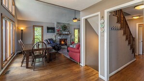 A spacious living area with a fireplace, wooden flooring, a dining table with chairs, a red sofa, and a staircase. - Aspen View (Blowing Rock)