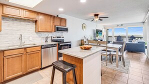 A modern kitchen with wooden cabinets, a central island, and a dining area with a view. - Gulfstream Condos Unit 603 | Beautiful Gulf Views | Pool, Hot Tub, BBQ (Corpus Christi)