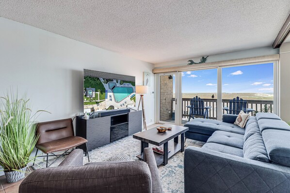 A balcony with a view of the beach, a sofa, a chair, a small table, and a potted plant.