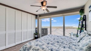 A bedroom with a bed, a ceiling fan, a view of the beach, and a balcony with plants. - Gulfstream Condos Unit 603 | Beautiful Gulf Views | Pool, Hot Tub, BBQ (Corpus Christi)