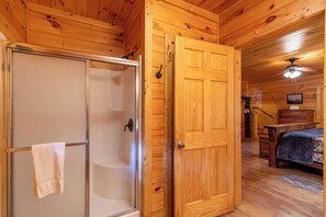 Ein Holzblock-Interieur mit einer Duschkabine aus Glas, einer Holztür, einem Bett und einem Deckenventilator.