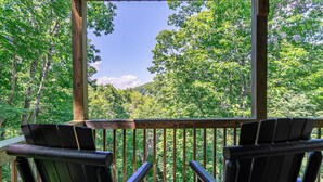 A wooden deck with two Adirondack chairs facing a forested hillside. - Another Point of View (Blowing Rock)