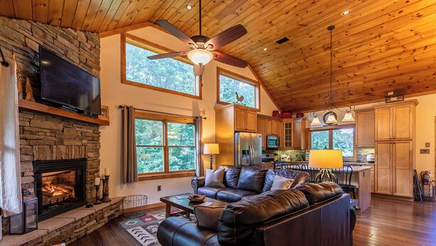 A spacious living room with a stone fireplace, leather sofa, and a large TV. - Another Point of View (Blowing Rock)