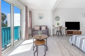 Ett modernt hotellrum med en balkong, en soffa, ett runt bord, en TV och en säng.
