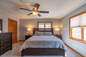 A bedroom with a bed, two bedside tables with lamps, a ceiling fan, a wooden dresser, and a window with blinds. - Hidden Heaven (Boone)