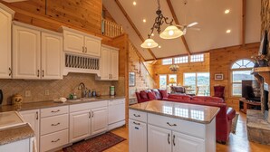 Een ruime keuken met witte kastjes, granieten aanrechtbladen en een centraal eiland. Er is een gezellige woonkamer met een rode bank en een open haard.