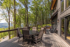 A deck with a table and chairs, surrounded by trees, overlooking a valley. - Howling at the Moon at Eagles Nest (Banner Elk)