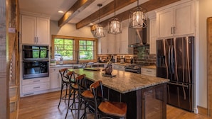 A spacious kitchen with a large island, stainless steel appliances, and a rustic wooden ceiling. - Howling at the Moon at Eagles Nest (Banner Elk)