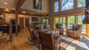 A spacious living room with a high ceiling, wooden beams, a large painting, and a view of the outdoors. - Howling at the Moon at Eagles Nest (Banner Elk)