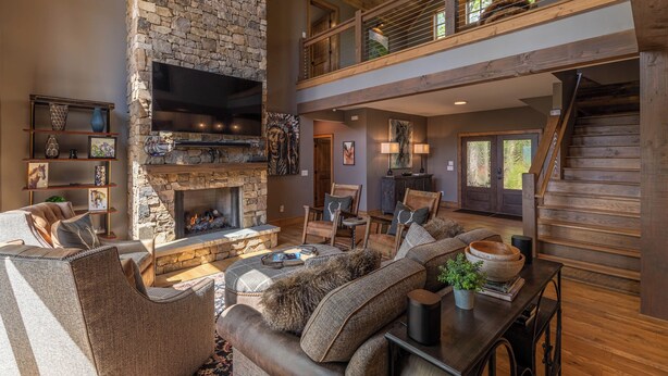 A spacious living room with a stone fireplace, comfortable seating, a flat-screen TV, and a wooden staircase leading to an upper level. - Howling at the Moon at Eagles Nest (Banner Elk)