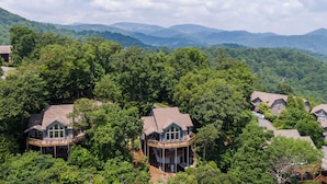 Un groupe de maisons entourées d’une forêt dense, avec des montagnes en arrière-plan.