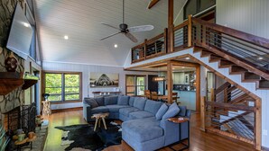 Ein geräumiges Wohnzimmer mit einem großen Ecksofa, einer Holztreppe und einem Steinkamin.
