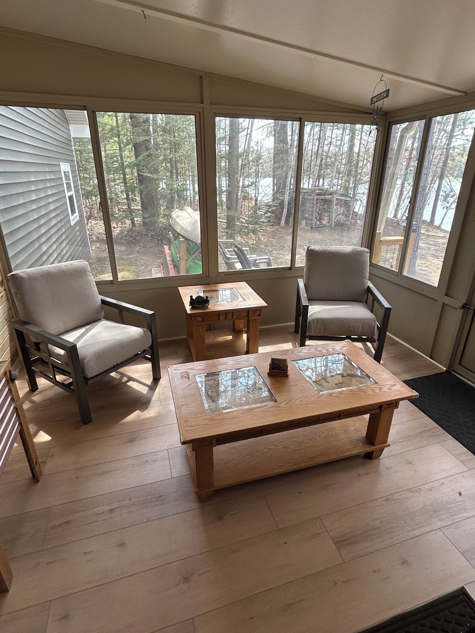 Une véranda avec deux fauteuils, une table basse et de grandes fenêtres donnant sur une zone boisée.