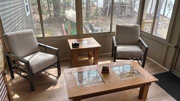 Une véranda avec deux fauteuils, une table basse et de grandes fenêtres donnant sur une zone boisée.