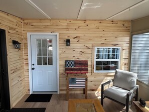 A room with wooden walls, a white door, a small table with an American flag, a chair, and a window. - The Resting Place on Lake Louise (Johannesburg)
