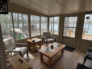 A sunroom with large windows, a wooden table, a chair, and a sofa. - The Resting Place on Lake Louise (Johannesburg)