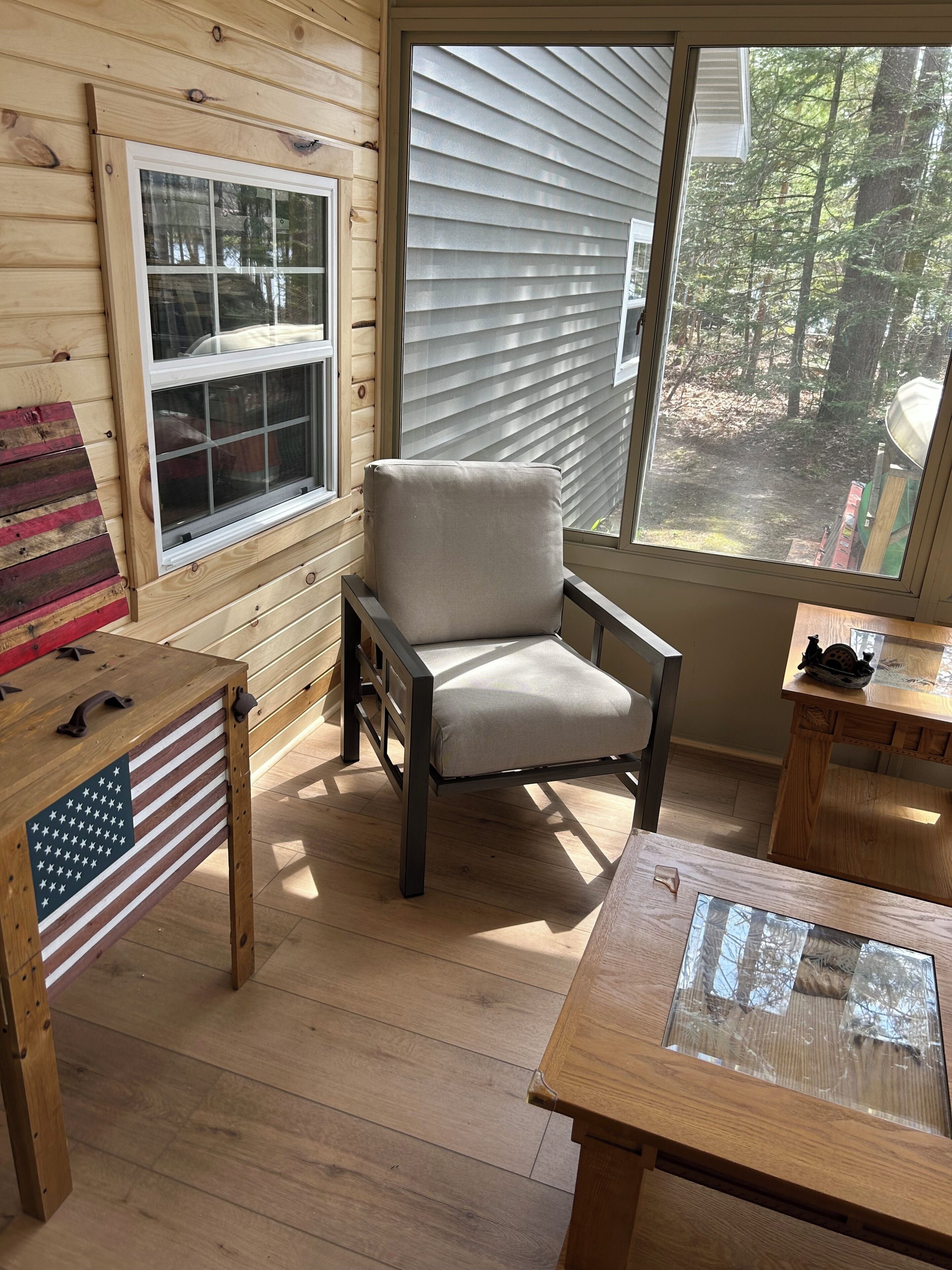 A wooden interior with a window, a cushioned chair, a table, and a flag-themed table.